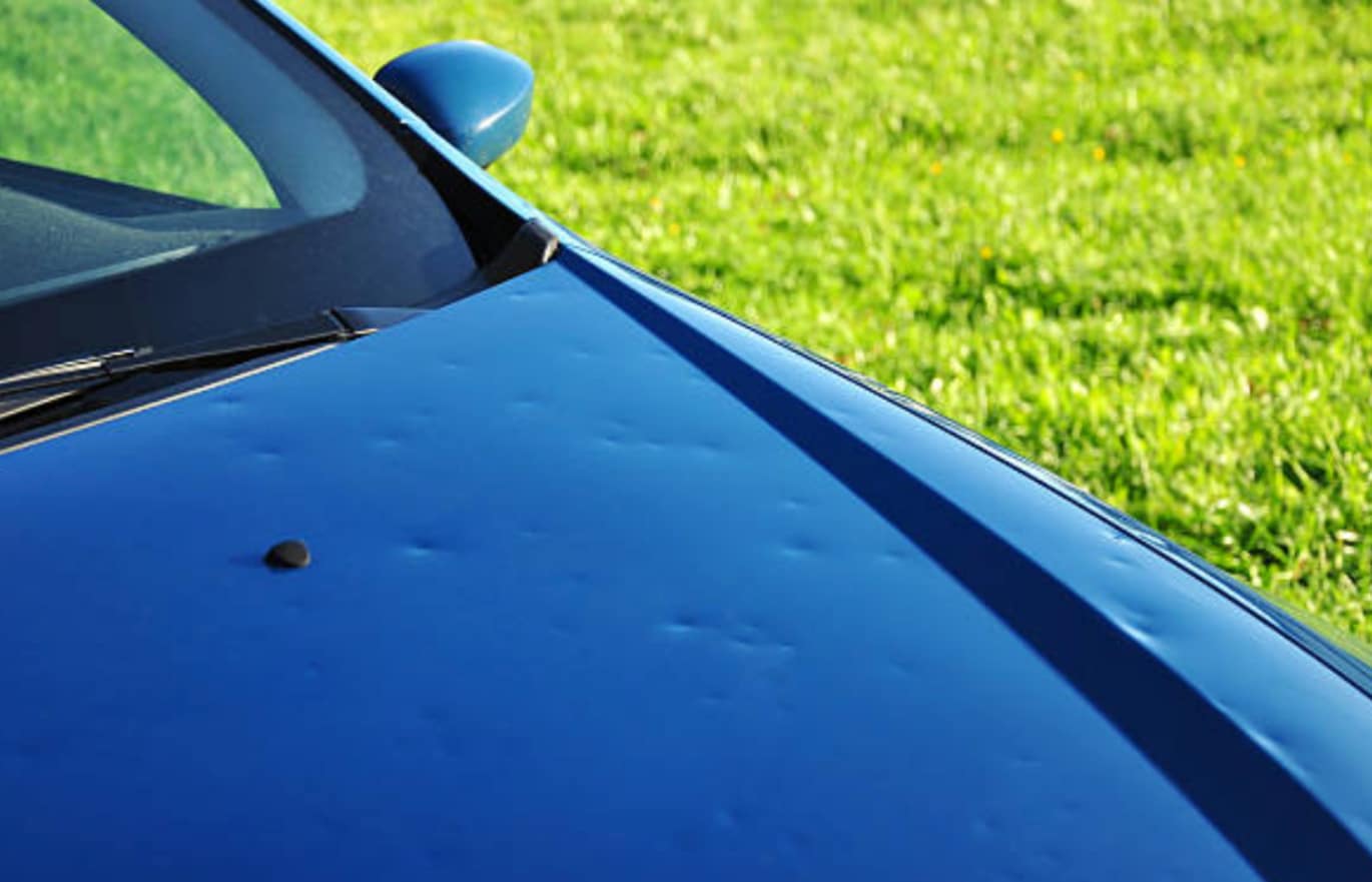 Capô de carro prata após chuva de granizo com múltiplos amassados sob luz natural