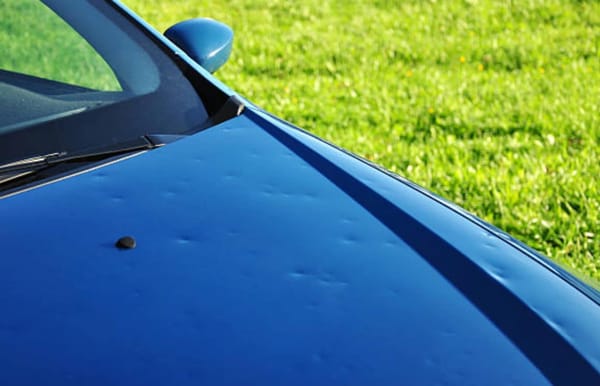 Capô de carro prata após chuva de granizo com múltiplos amassados sob luz natural